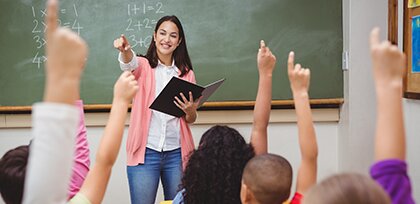 math teacher at front of the room pointing at students with hands raised